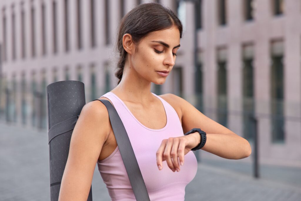 outdoor-shot-active-young-woman-checks-fitness-results-fitness-watch-carries-karemat-dressed-sportswear