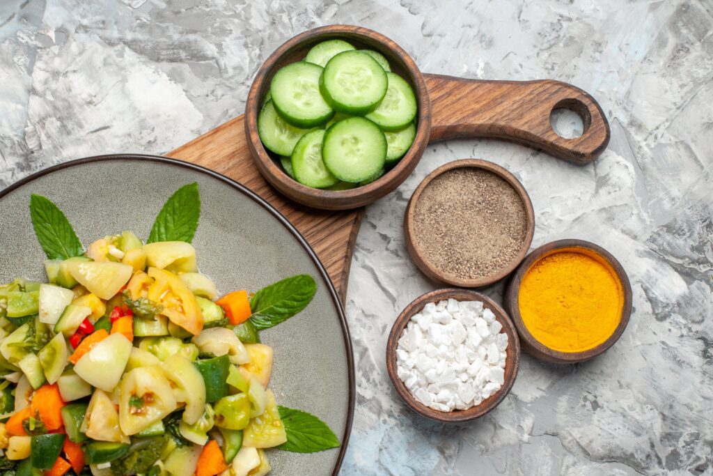 top-view-green-tomato-salad-oval-plate-cutting-board-different-spices-dark-background