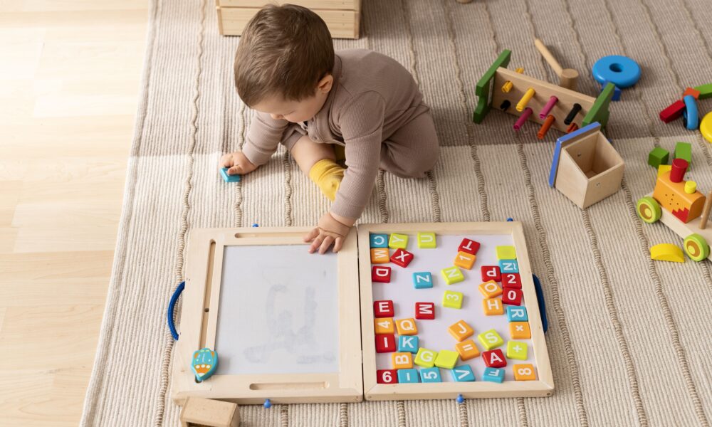 A collection of simple, screen-free kids activities like playdough, books, and building blocks laid out on a wooden floor.