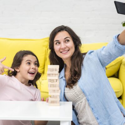 The 10-Minute Miracle: How This Simple Habit Transformed My Chaotic Home A tired but happy mother and daughter laughing together while building a block tower on the living room floor.