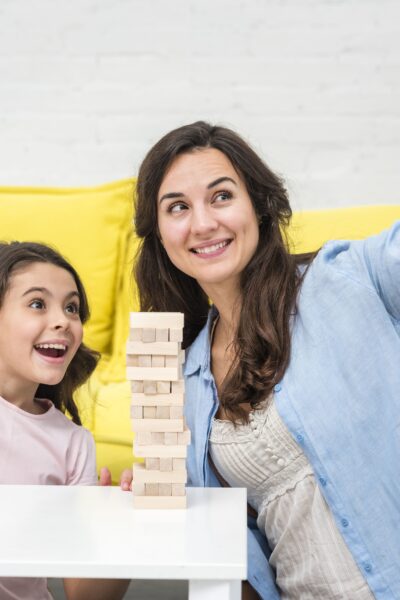 The 10-Minute Miracle: How This Simple Habit Transformed My Chaotic Home A tired but happy mother and daughter laughing together while building a block tower on the living room floor.